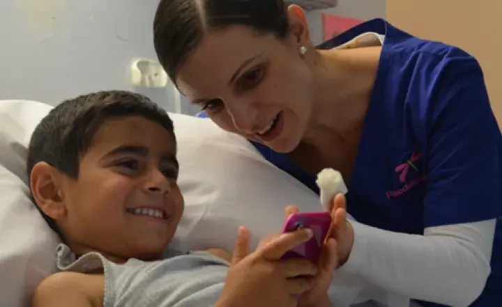 A nurse smiles at a boy playing in a hospital bed